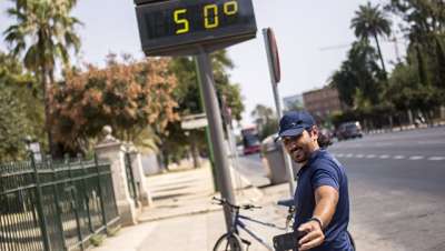 Мужчина фотографируется у электронного табло, которое показывает температуру +50 градусов по Цельсию на улицах города Севилья в Испании © РИА Новости / Алехандро Мартинез Велез